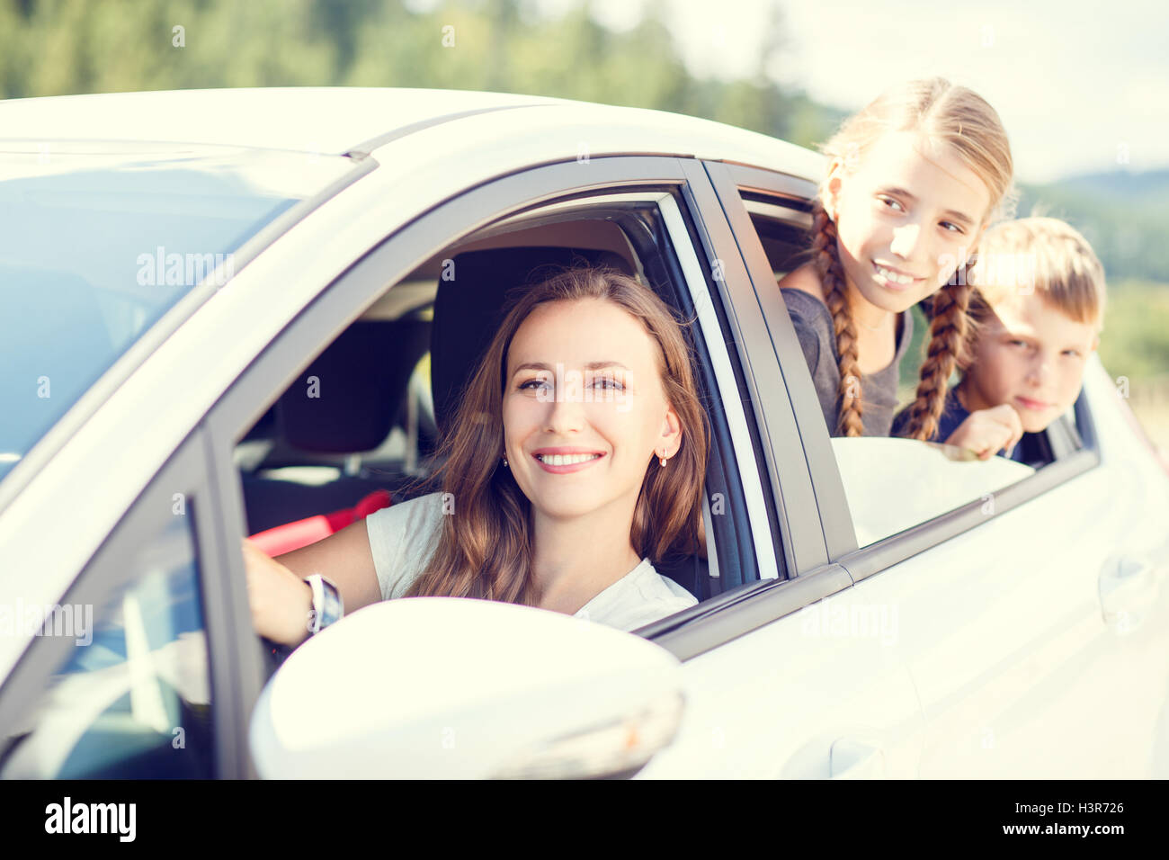 Happy young woman and her children sitting in a car and look out from windows. Family travel warm color toned image Stock Photo