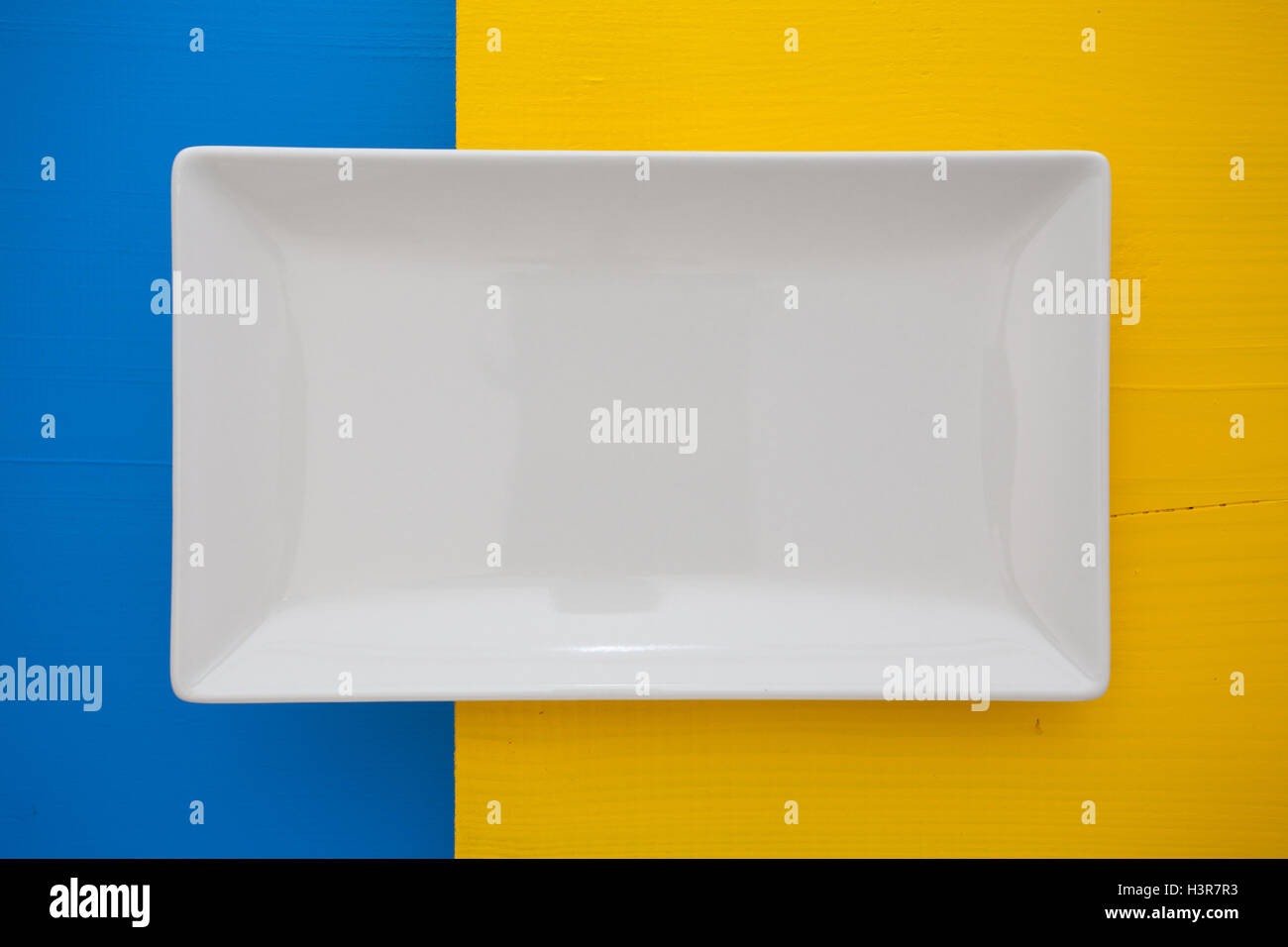 Empty white ceramic dish on over blue and yellow wooden table ...