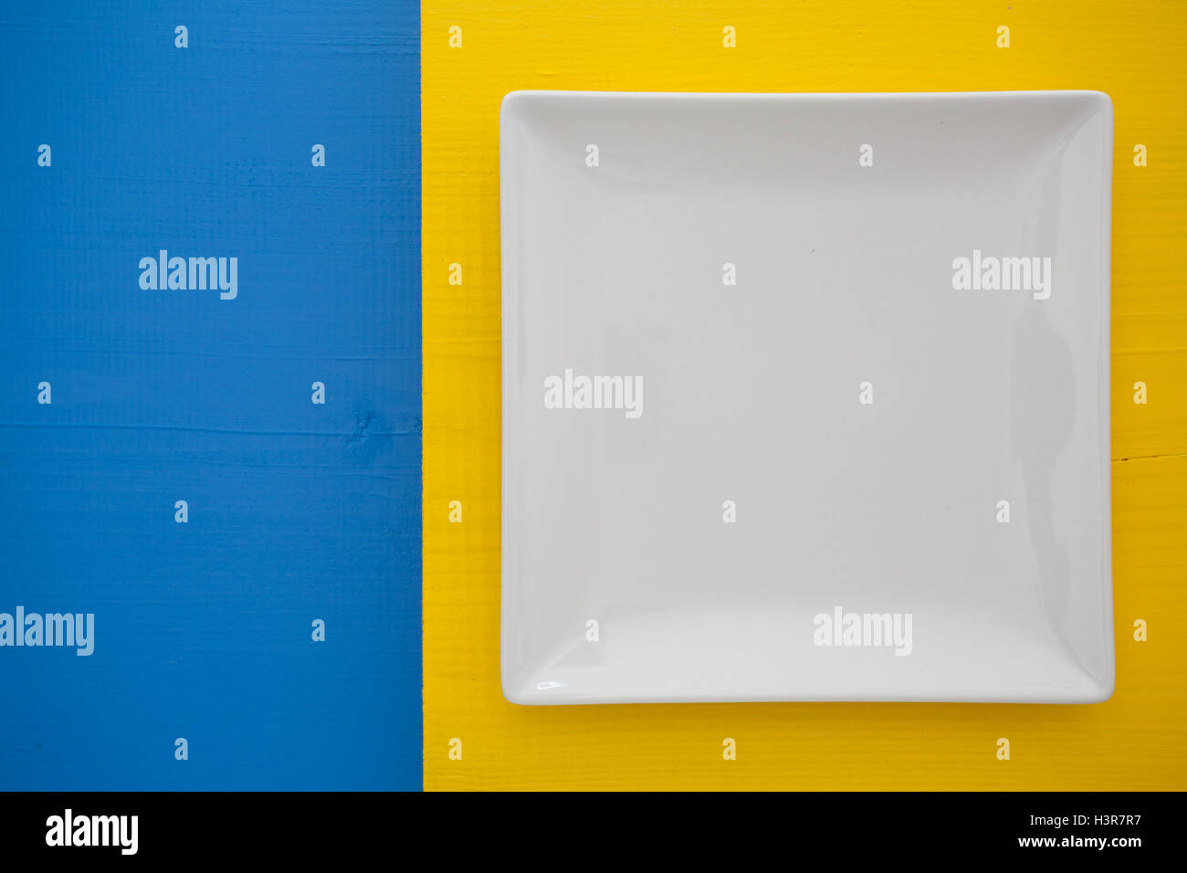 Empty white ceramic dish on over blue and yellow wooden table, square ...