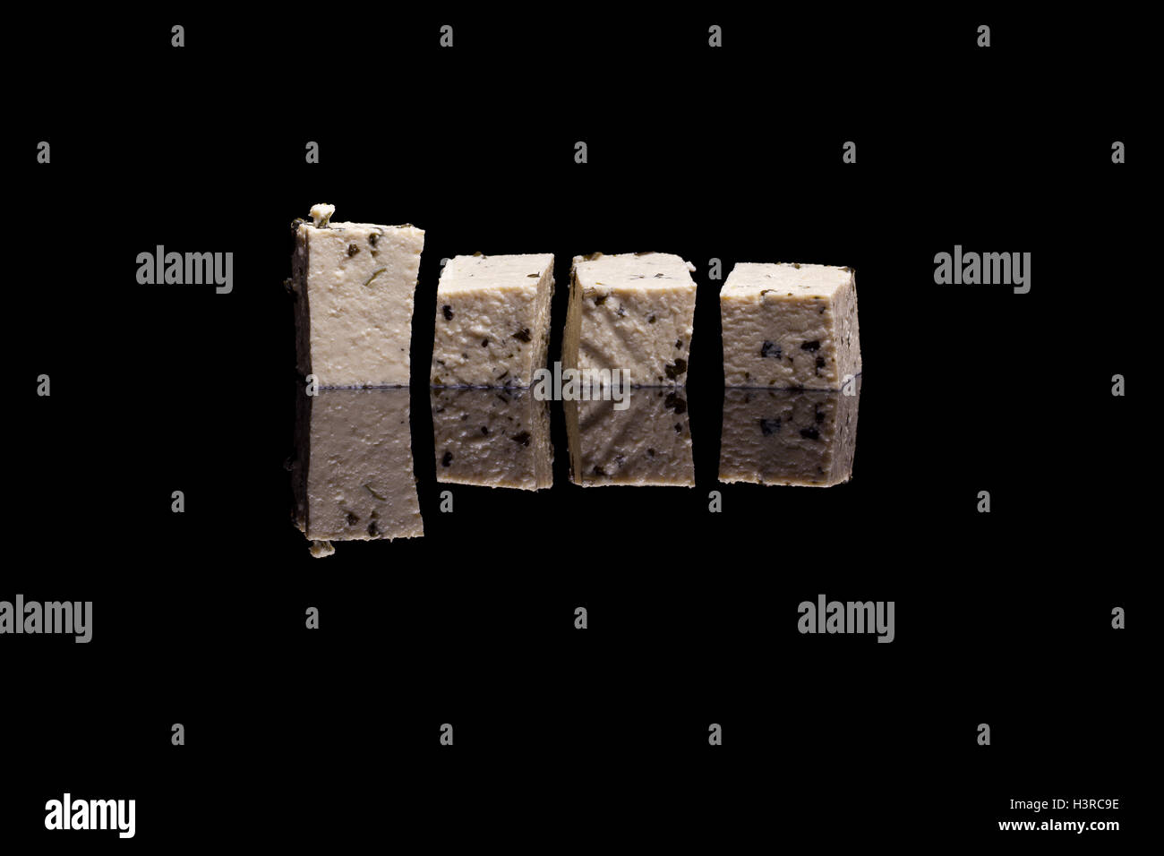 Four cubes of tofu with basil isolated on black reflective background Stock Photo