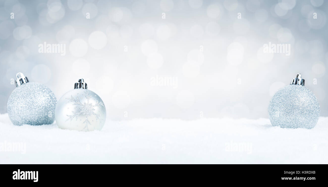 Silver Christmas baubles on snow with defocused silver and white lights ...