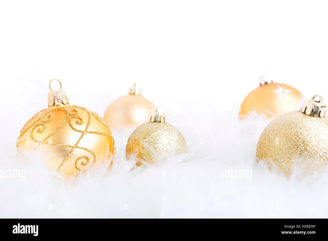 Golden Christmas baubles on a soft feathery surface with a white background. Stock Photo
