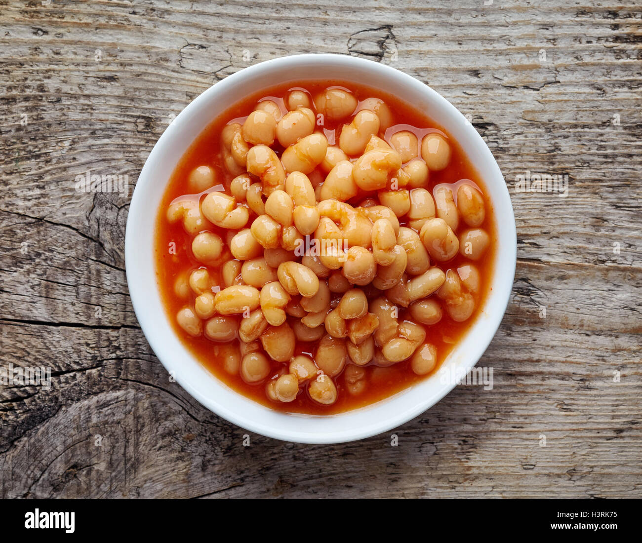 White bowl of beans in tomato sauce on wooden table, top view Stock Photo