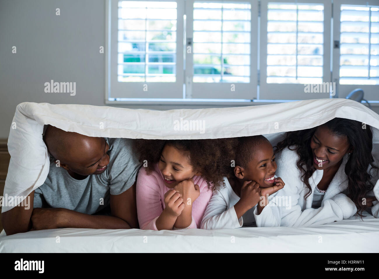Happy family lying under a blanket on bed Stock Photo Alamy
