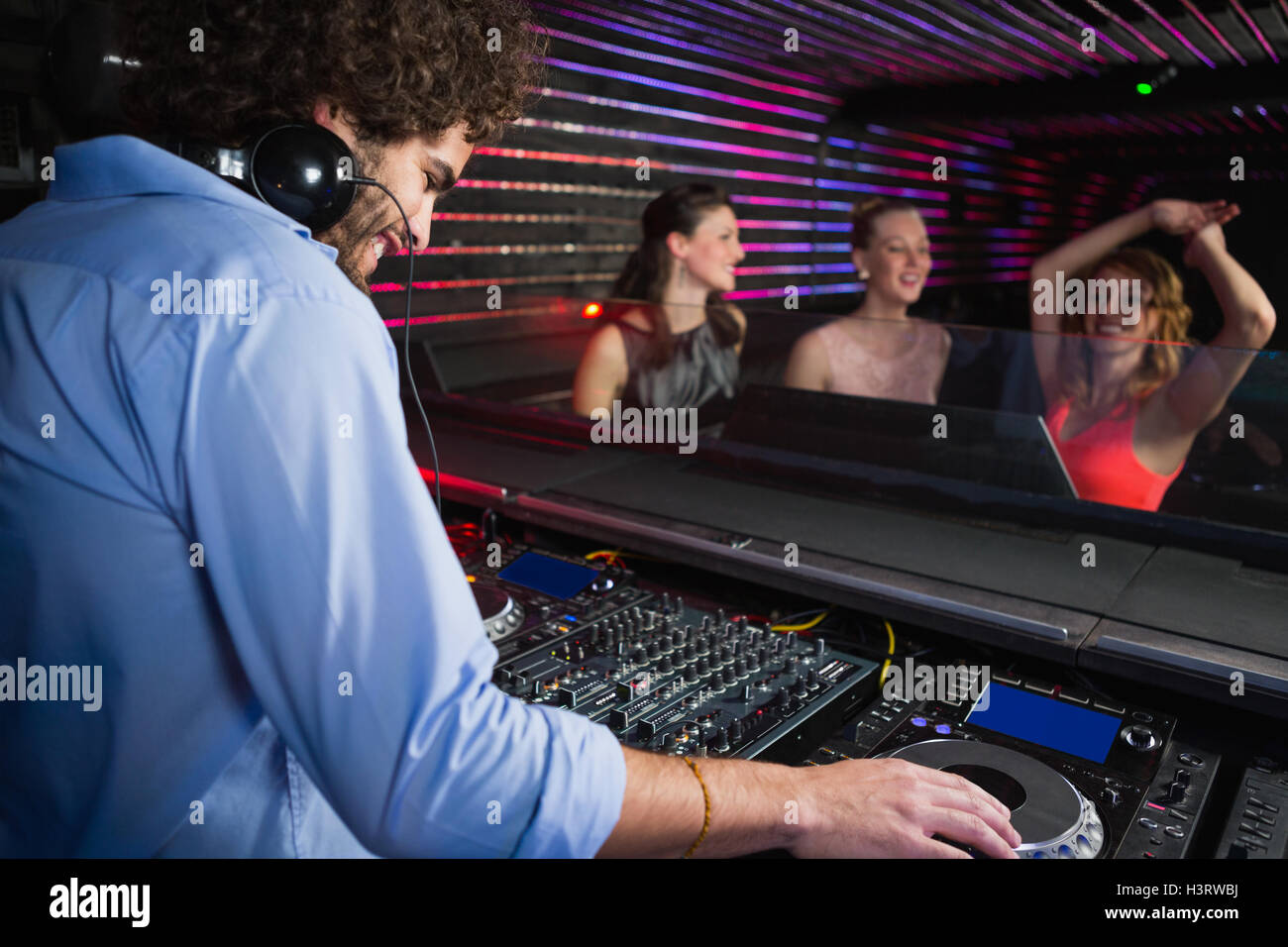 Male disc jockey playing music with three women dancing on the dance