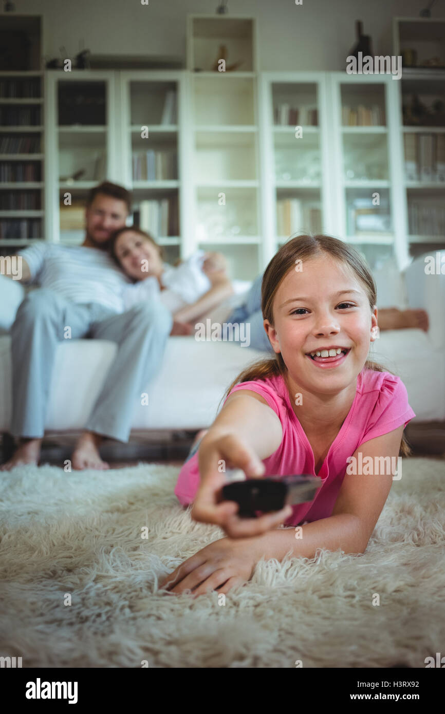 Smiling girl lying on rug and changing channels Stock Photo
