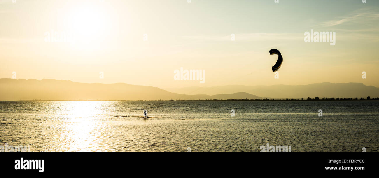 A person doing kitesurf in a calmed bay at sunset. Stock Photo