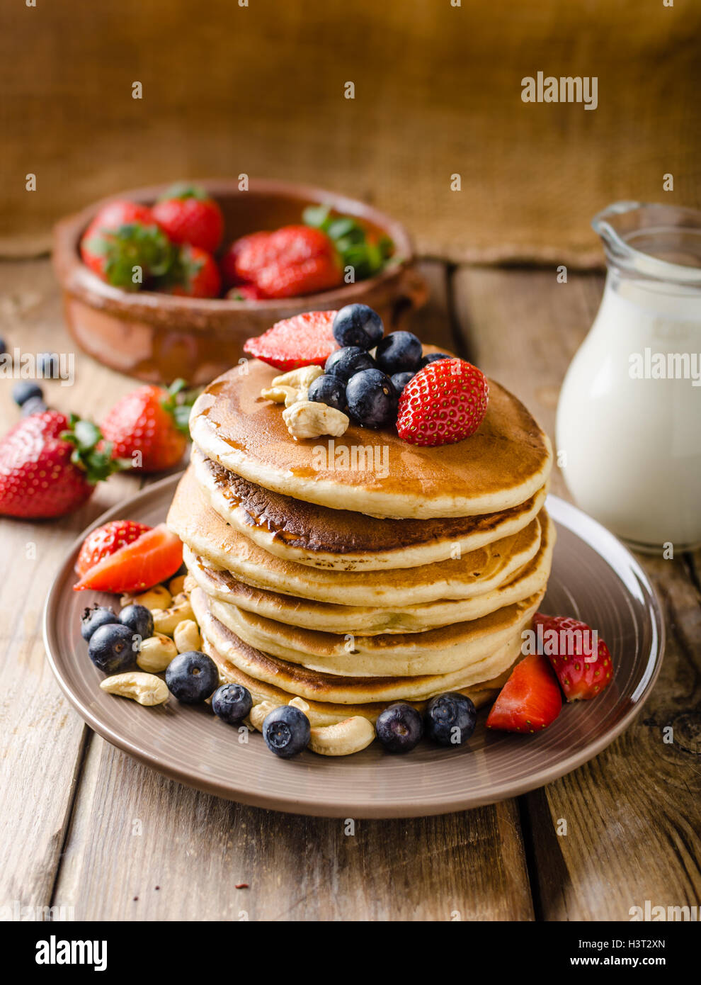 Original american pancakes with berries, roasted nuts and milk behind,  rustic style photo, place for advertisment Stock Photo - Alamy
