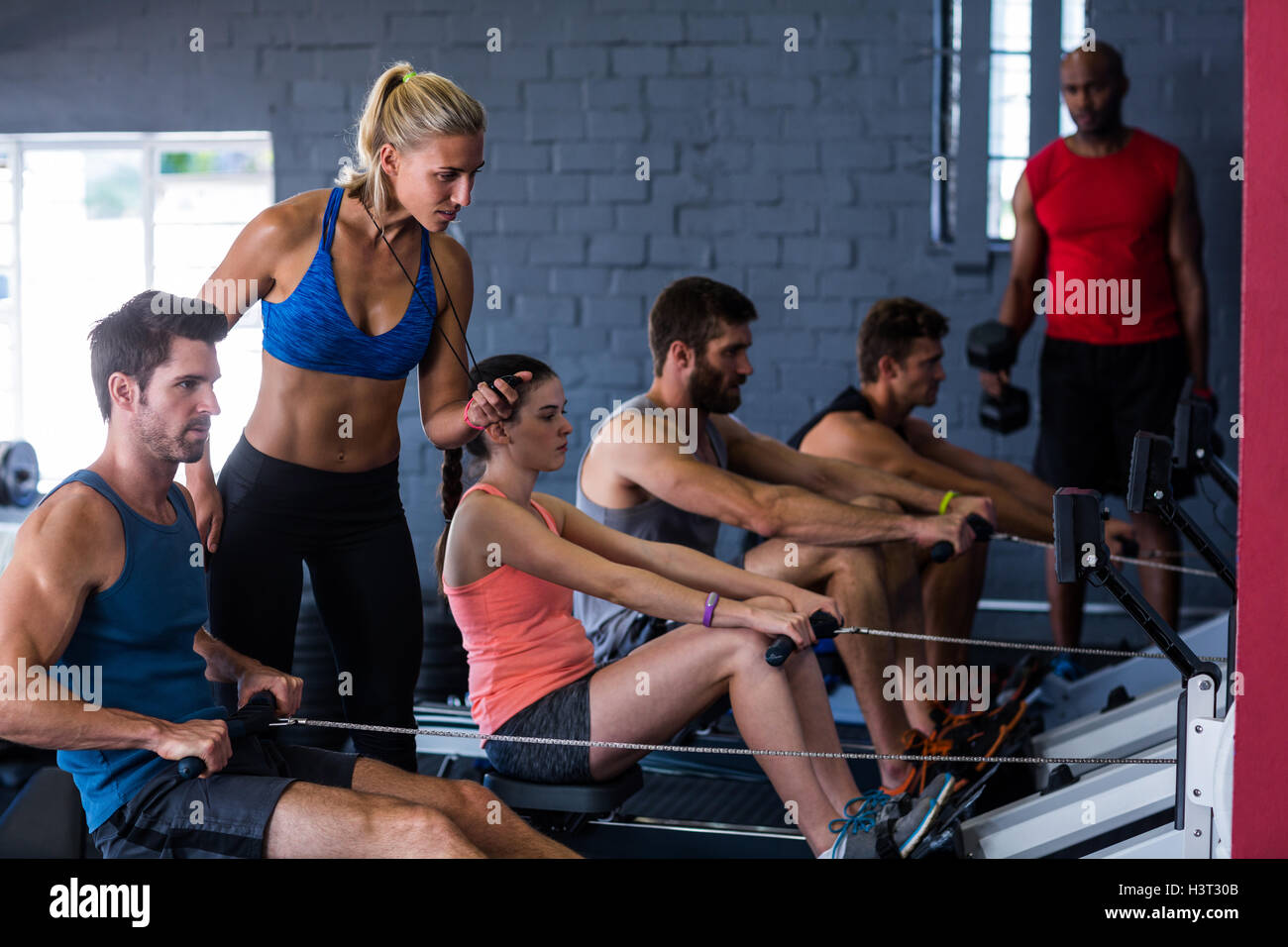 People using rowing machine with fitness instructor in gym Stock Photo