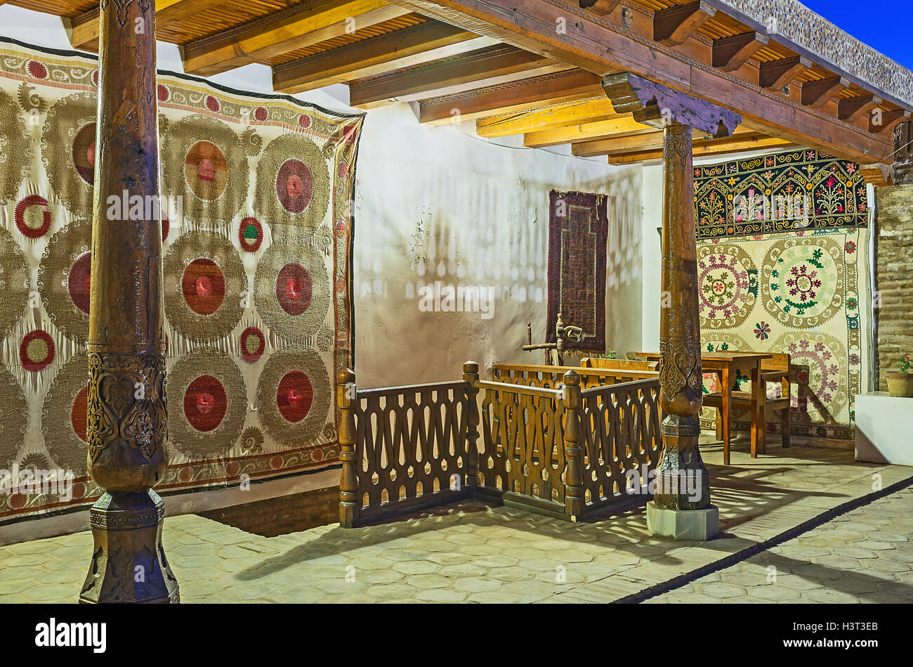 The Caravan Saray terrace decorated with traditional silk carpets and wooden pillars in Bukhara. Stock Photo