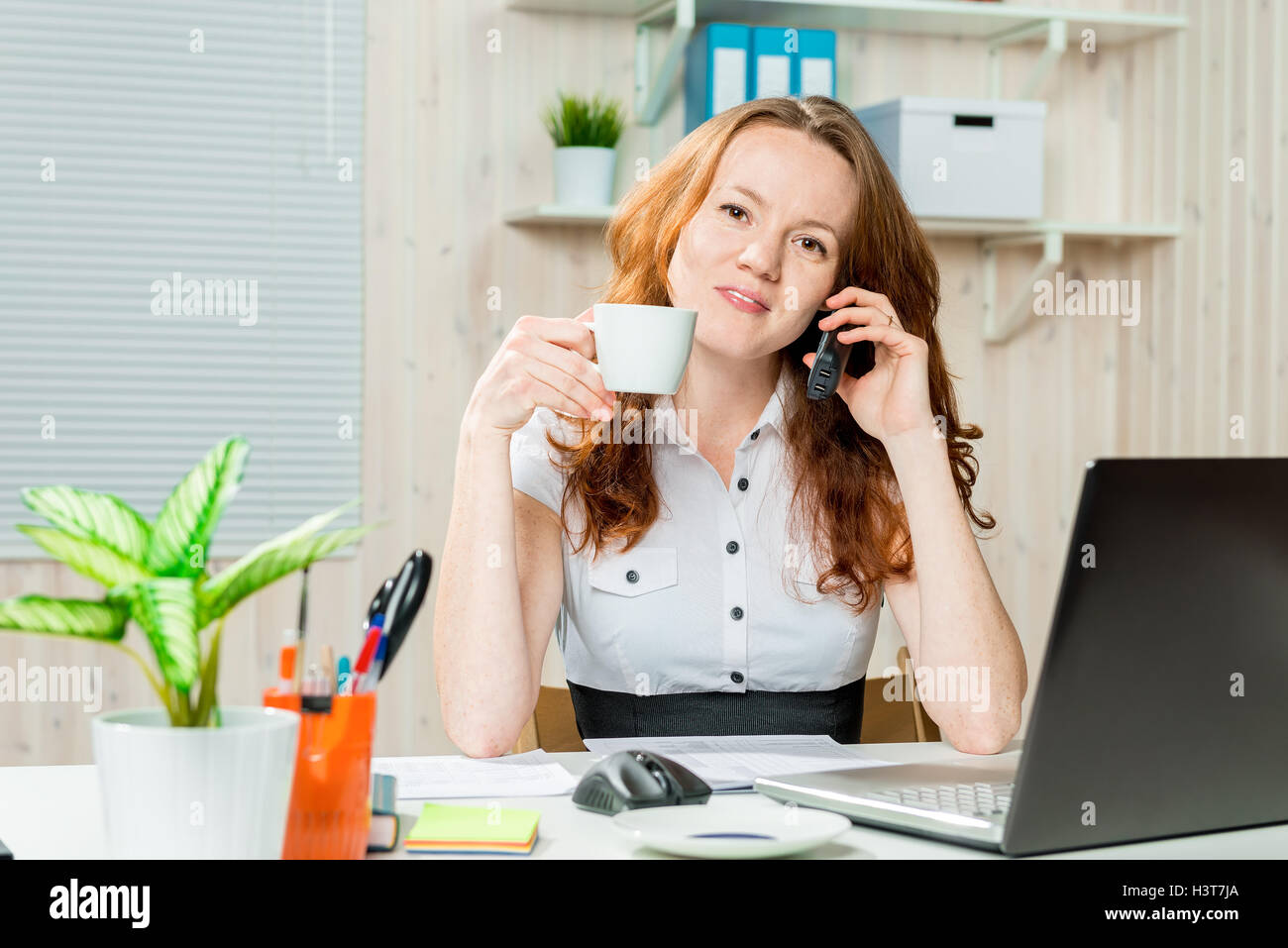 woman in the office at work with a cup of coffee and a telephone Stock