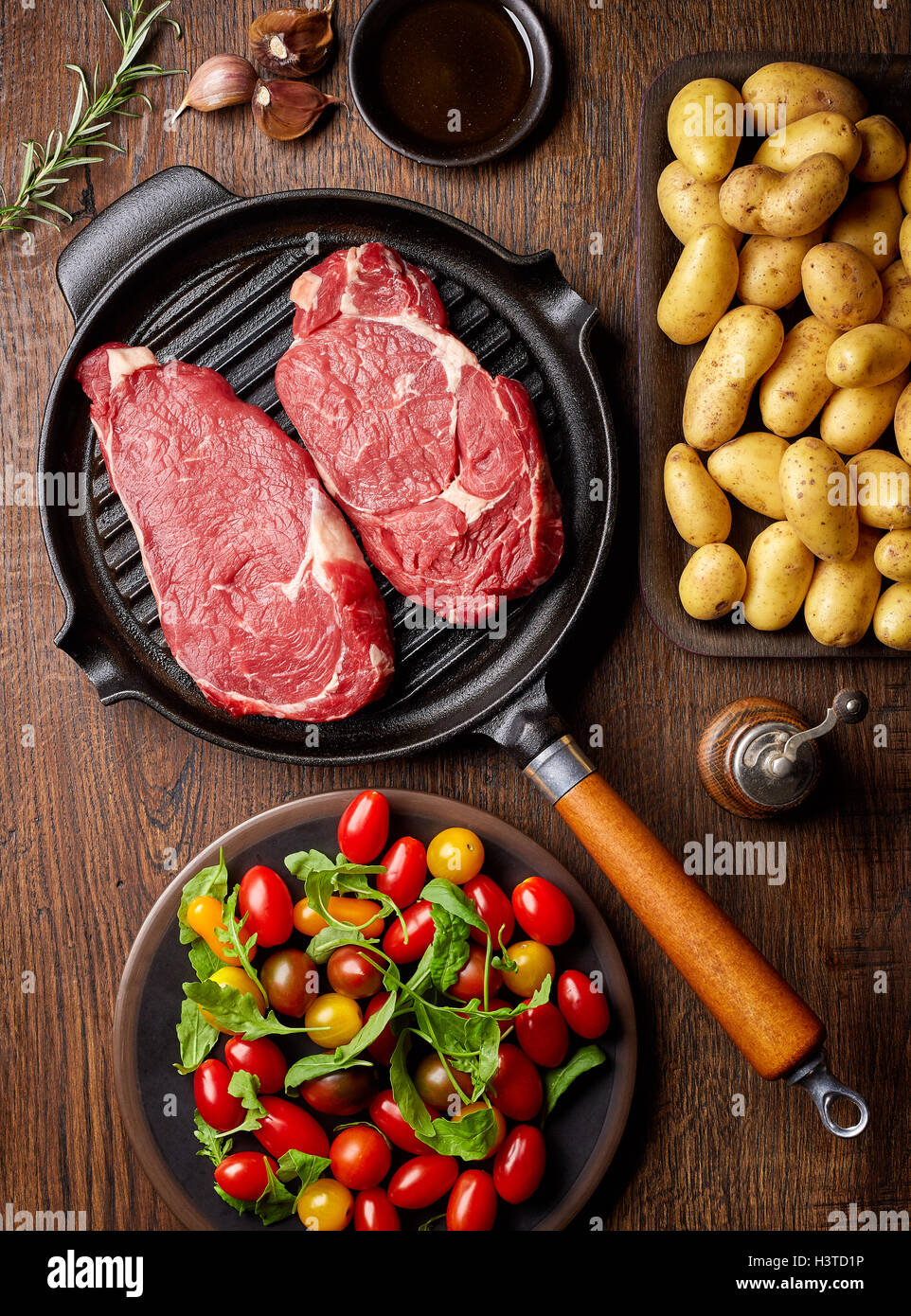 Raw beef steak on grill pan, potatoes, spices and tomatoes, top view, on wooden table Stock Photo