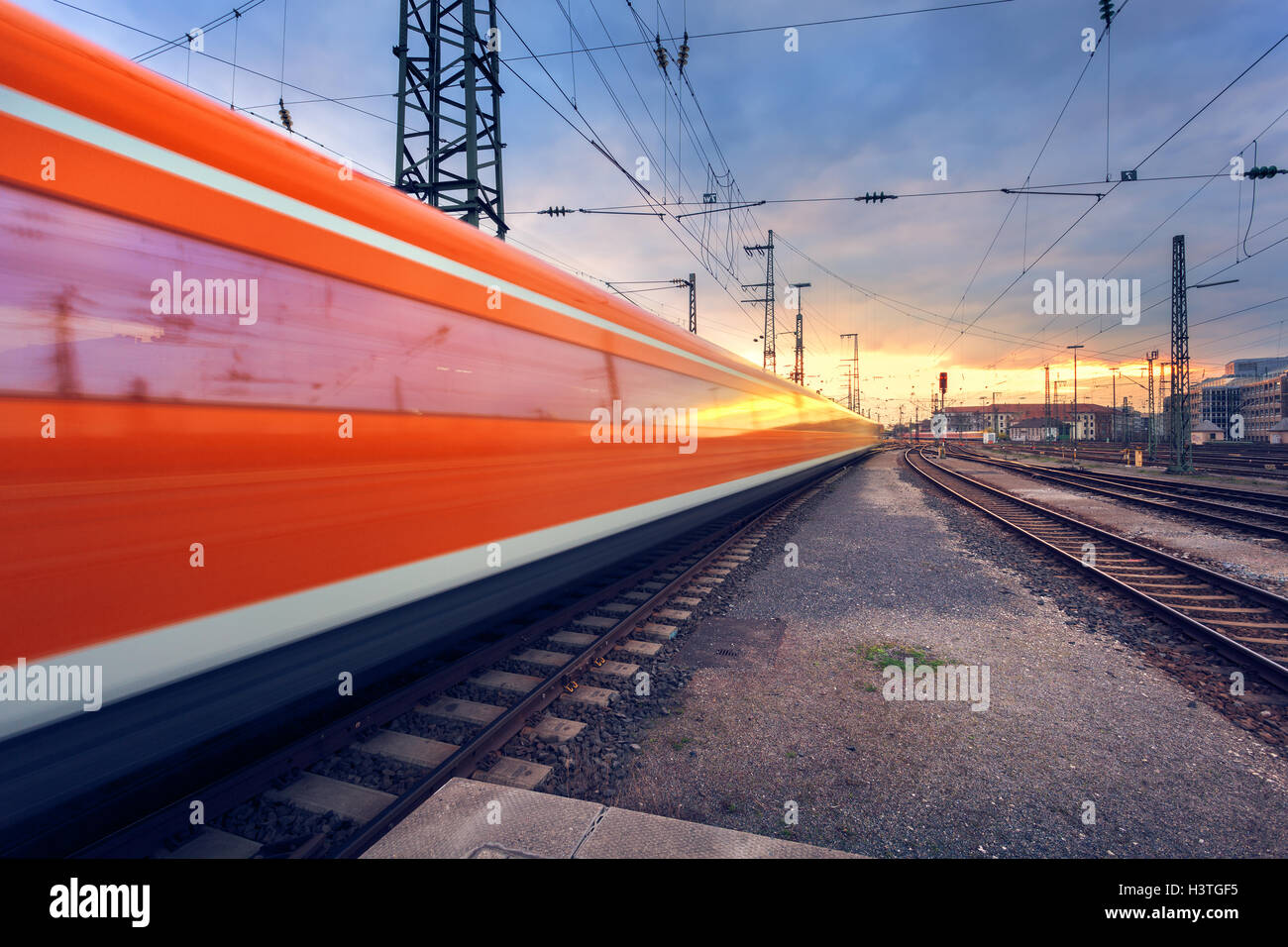 High speed red passenger train on railroad track in motion at sunset