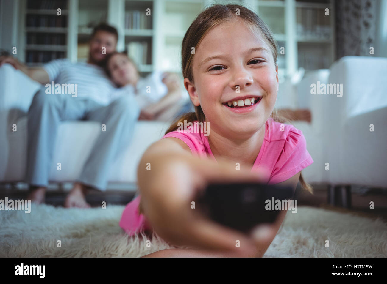 Smiling girl lying on rug and changing channels Stock Photo