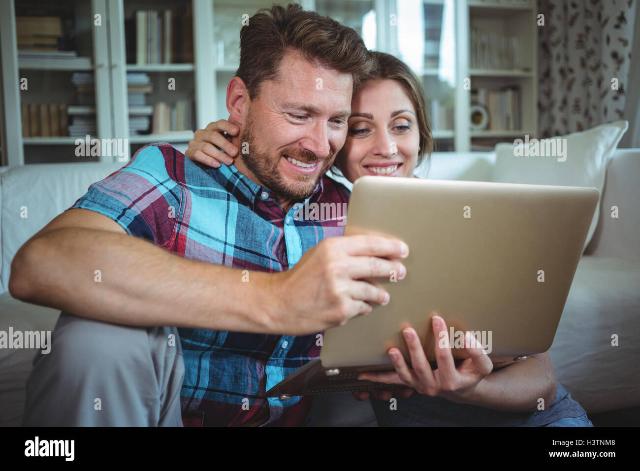 Happy couple using laptop in living room Stock Photo - Alamy