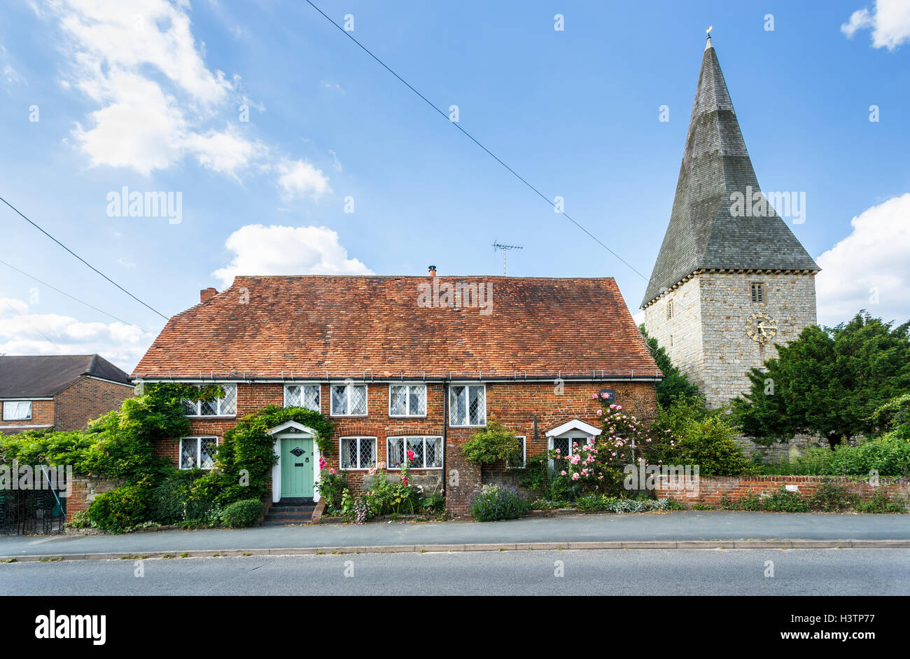 Fourteenth century cottage and St Peter's church spire in Ash near Guildford, Surrey with hollyhocks, roses around the windows Stock Photo