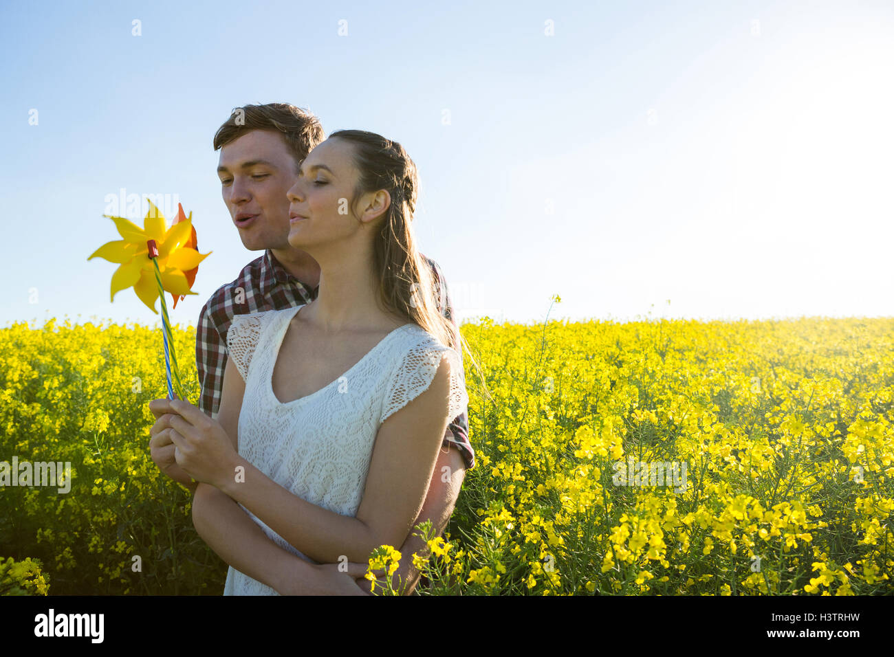 Couple holding blowing pinwheel in mustard field Stock Photo