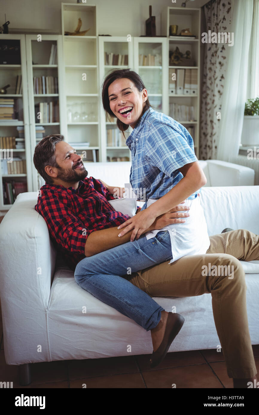 Happy woman sitting on mans lap in living room Stock Photo