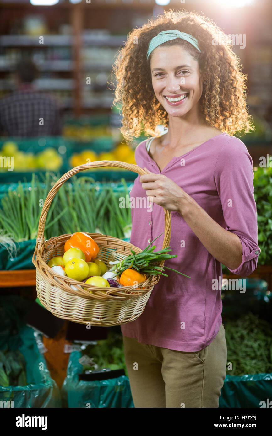 Smiling woman holding basket of vegetables in organic section Stock ...