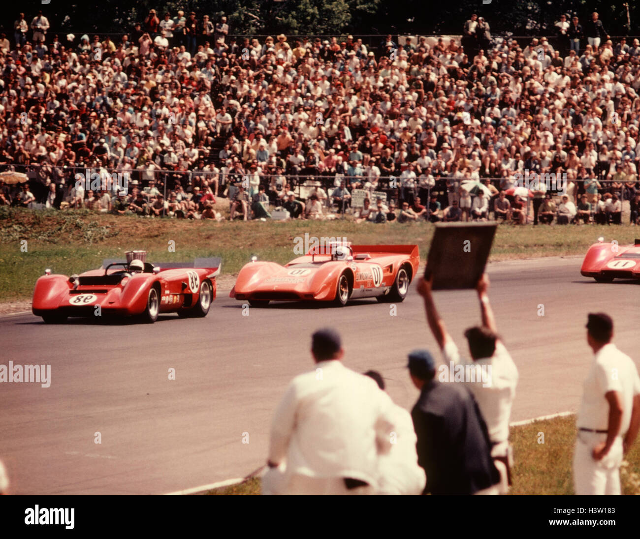 1970s CAR AUTO RACING 3 RED CARS TRACK MAN PIT HOLDING UP SIGN TO DRIVERS Stock Photo