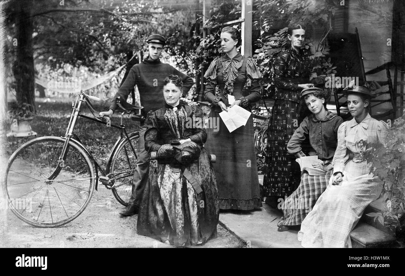 1890s GROUP PORTRAIT FIVE WOMEN ONE MAN STANDING BY BICYCLE POSING ON FRONT PORCH OF HOUSE LOOKING AT CAMERA Stock Photo