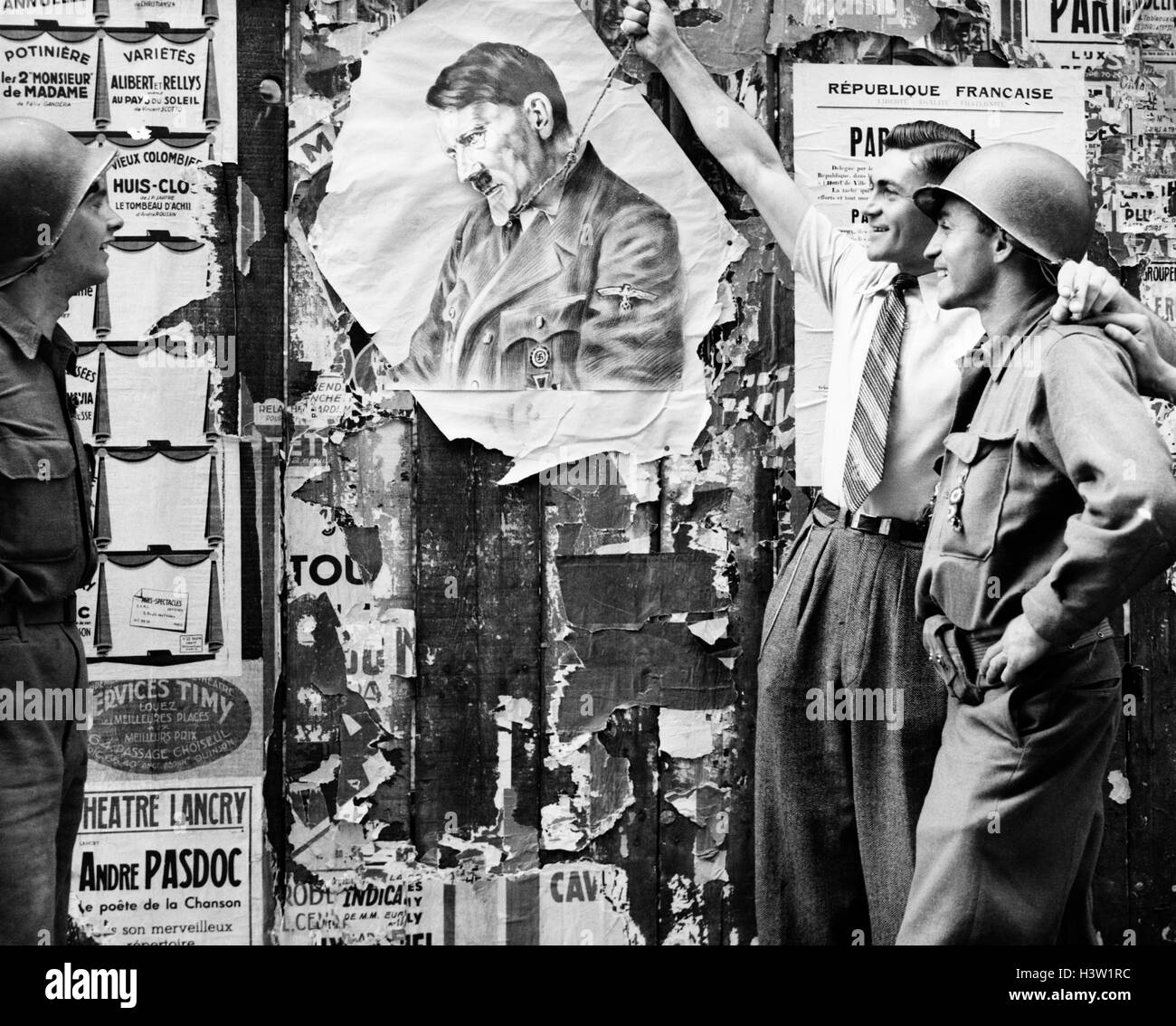 1940s CIVILIAN MAN SYMBOLICALLY HANGING ADOLF HITLER AS TWO YANK SOLDIERS LOOK ON AUGUST 26 1944 IN LATIN QUARTER PARIS FRANCE Stock Photo