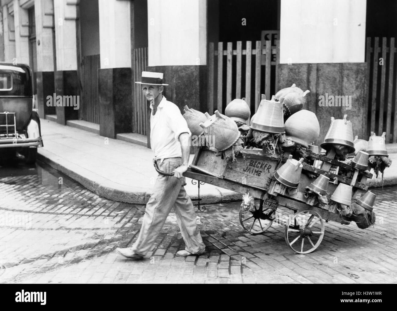 1930s 1940s POT SALESMAN LOOKING AT CAMERA PULLING HIS CART FULL OF CLAY POTS ON STREET HAVANA CUBA Stock Photo