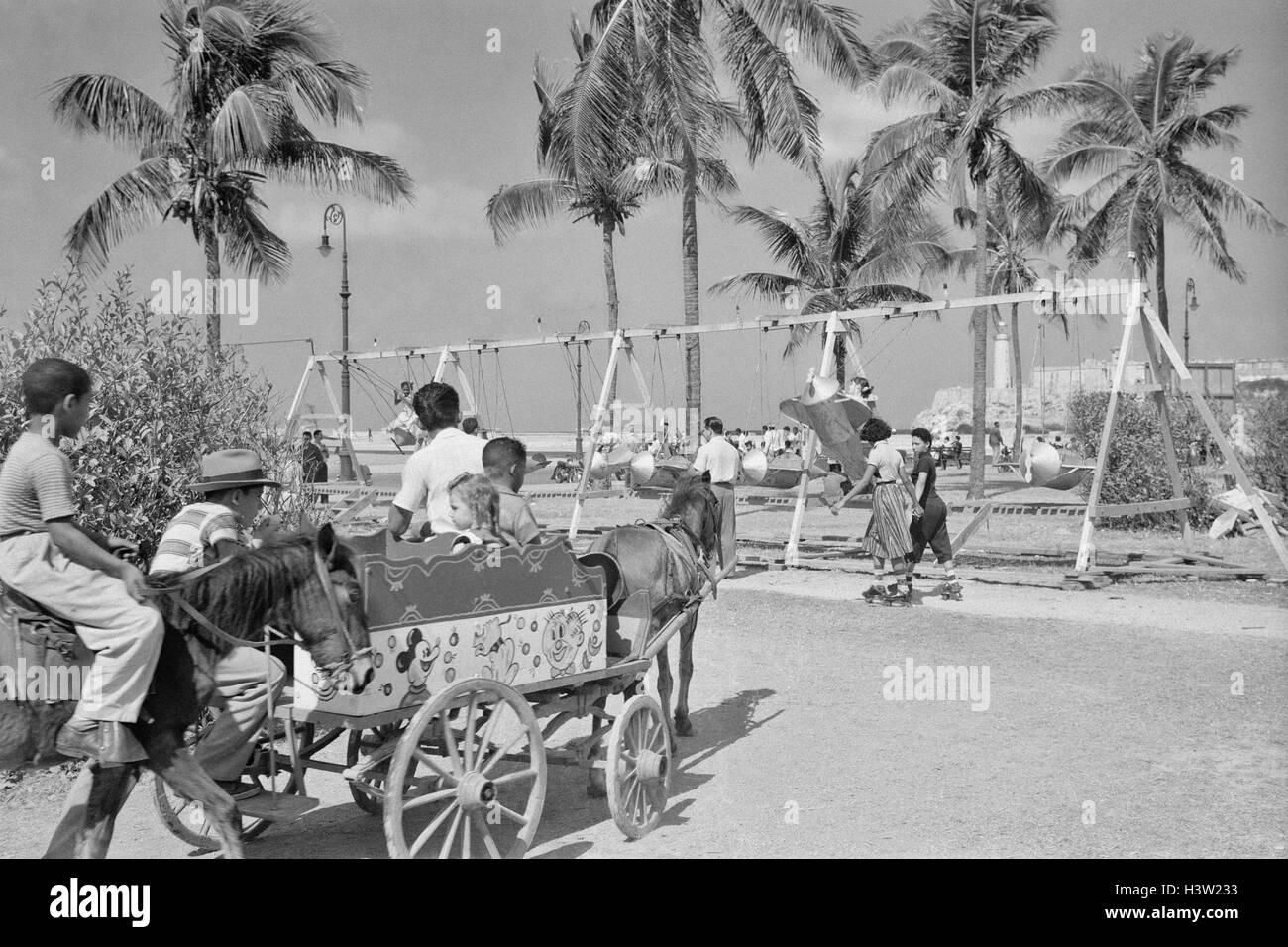 1950s CHILDREN ON PLAYGROUND AND CARNIVAL ON MALECON PARKWAY HAVANA CUBA Stock Photo