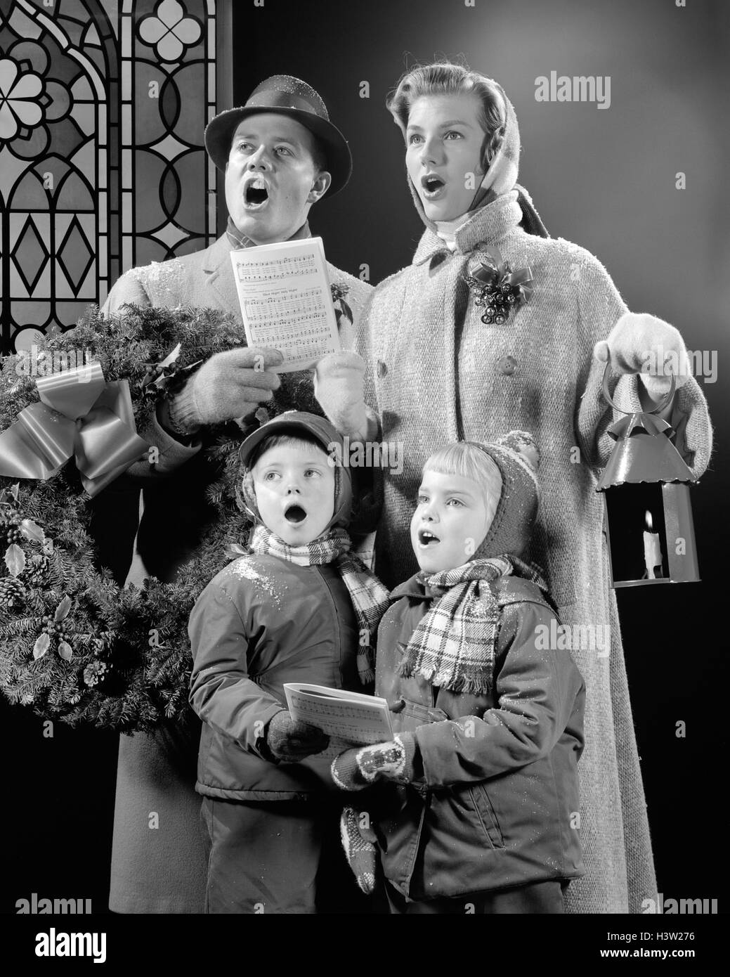 1950s FAMILY OF FOUR SON DAUGHTER SINGING CHRISTMAS CAROLS DAD HOLDING WREATH MOM HOLDING CANDLE LANTERN Stock Photo - Alamy