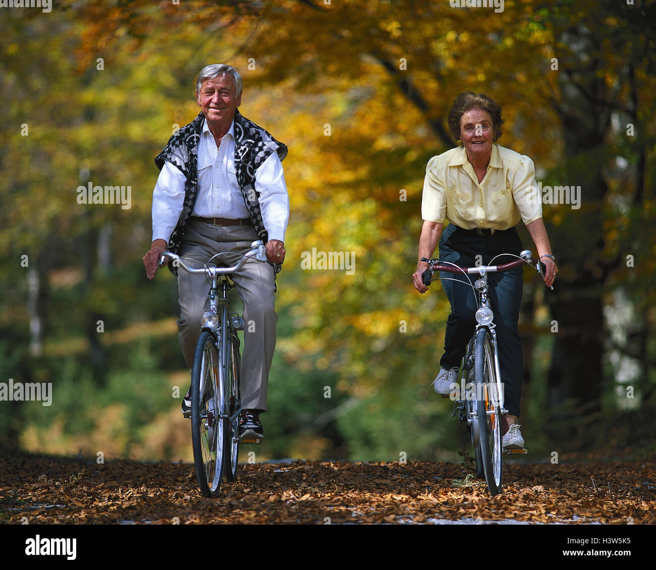 Senior couple riding of a bike autumn senior citizens pensioners couple forest way bicycles activity seasons autumn foliage enterprise cycling tour actively fit agile actively healthy sport leisure ti...