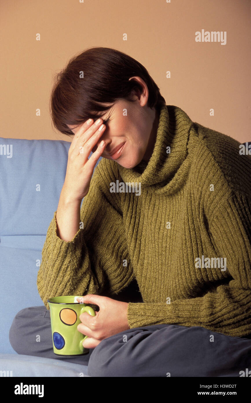 Sofa, woman, young, teacup, gesture, cephalalgias 30 years, 30-40 years, tea drink, coffee cup, coffee drinking, cup, hold, disease, ill, of a headache, pain, pains, migraine, migraine attack, cephalalgia, thrashing, painfully, annoyance, stress, ailment, Stock Photo