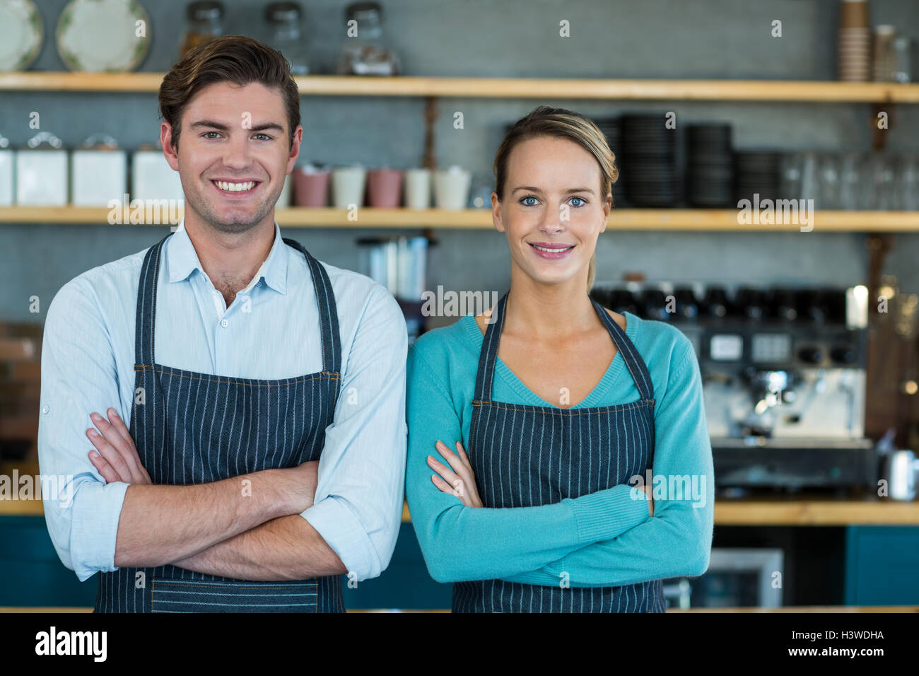 Portrait of smiling waiter and waitress standing with arms crossed ...