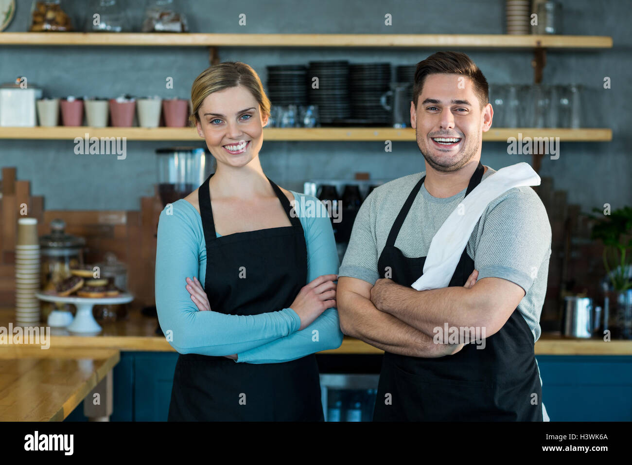 Portrait of smiling waiter and waitress standing with arms crossed ...