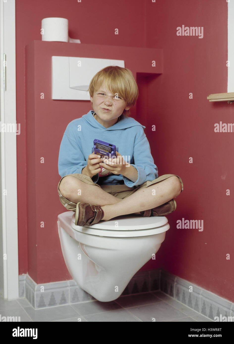 Toilet, boy, Gameboy, play, inside, bath, bathroom, child, 7 years, leisure time, childhood, gambling addiction, game, pouch computer, computer game, nose, to bodies, grimace, dissatisfied, discontent, expression Stock Photo