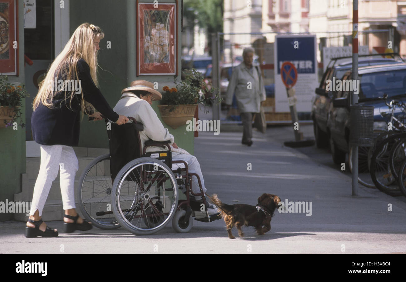 Town, young woman pushes invalid's wheel chair with senior, dachshund! only editorially! Dog, old, granddaughter, grandmother, ill Stock Photo