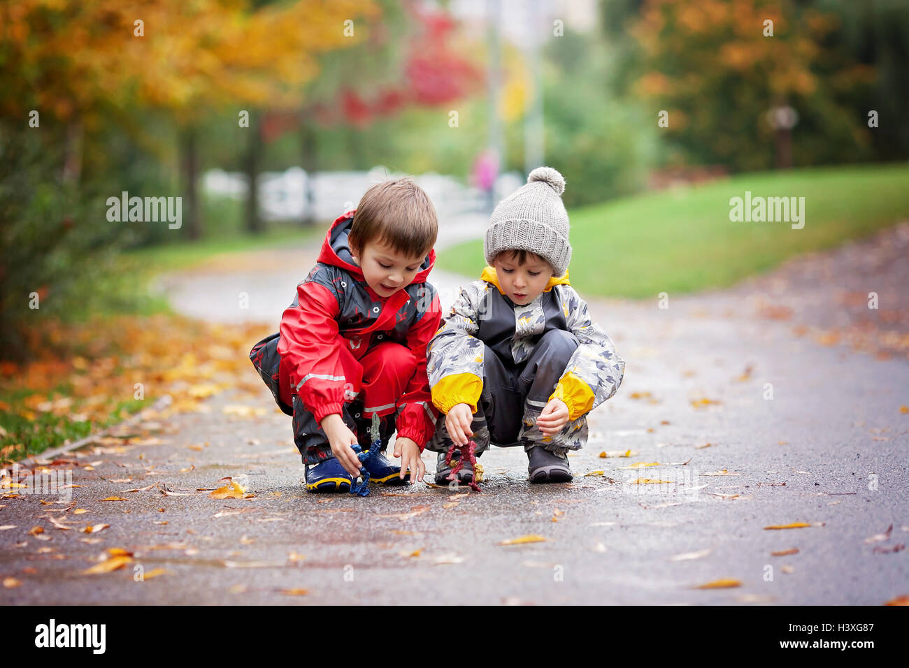Two children, playing together with toys in the park on a rainy day, autumn time Stock Photo