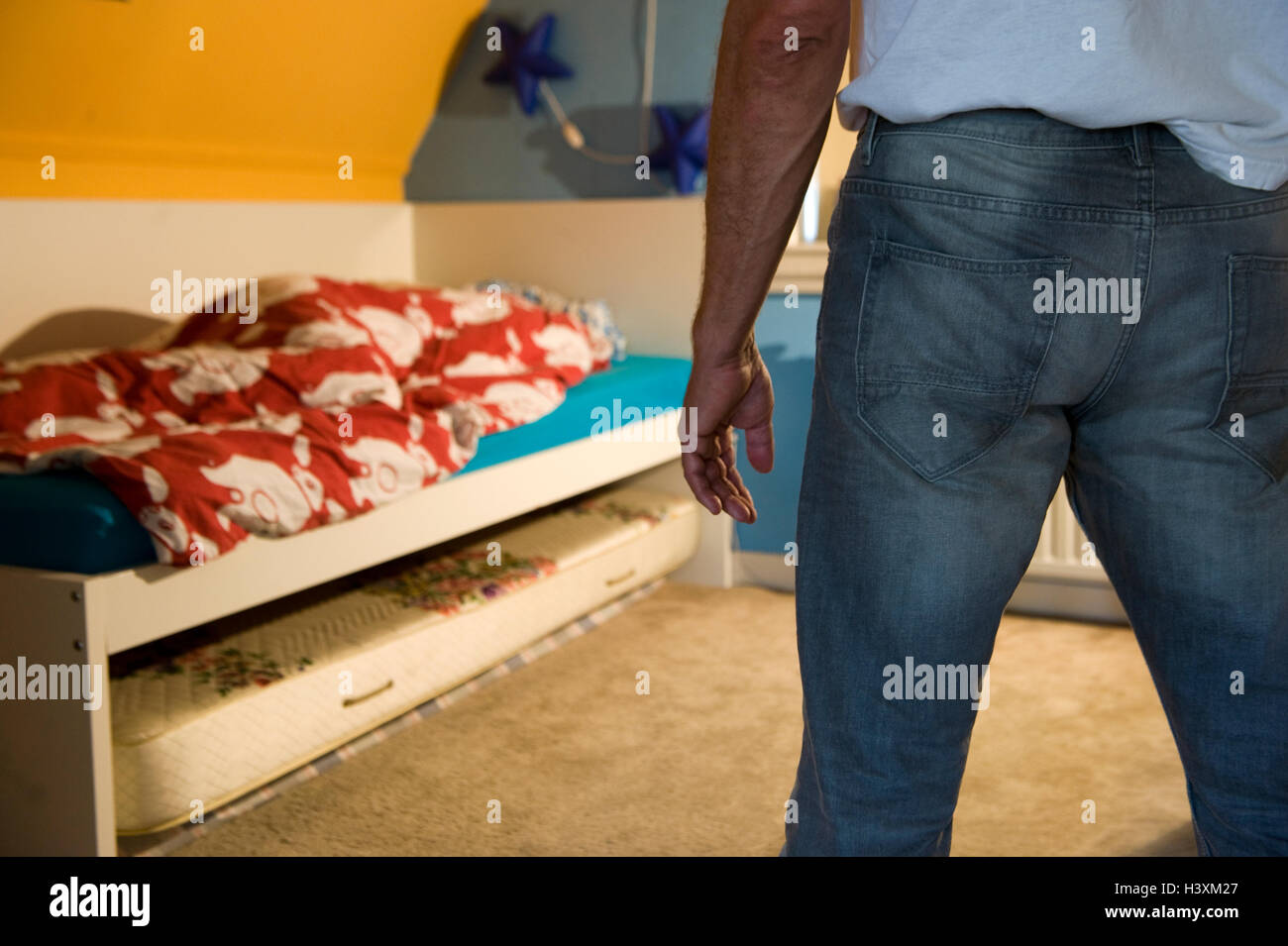 A father is standing in the bedroom of his child, while the kid hiding under the comforter Stock Photo