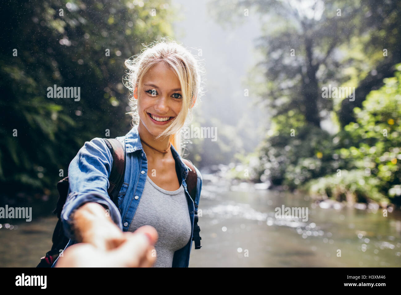 Smiling young woman holding man's hand and leading him in the forest hike. Point of view shot of couple by the creek. Stock Photo