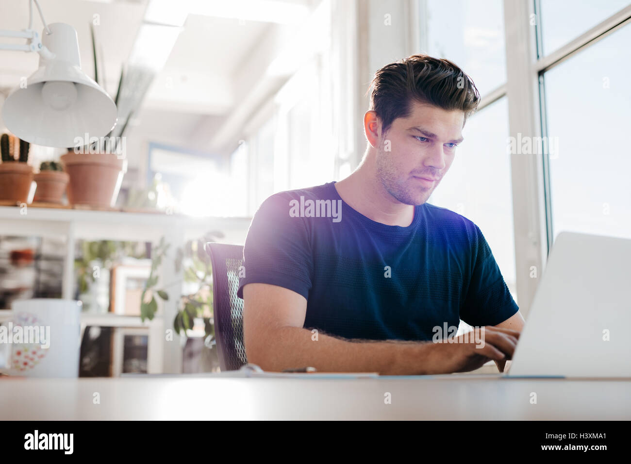 Young businessman using laptop computer in office. Young male executive working on laptop at his desk. Stock Photo