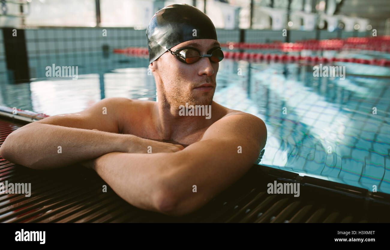 Shot of young man on the edge of pool relaxing and looking away. Professional male swimmer resting. Stock Photo