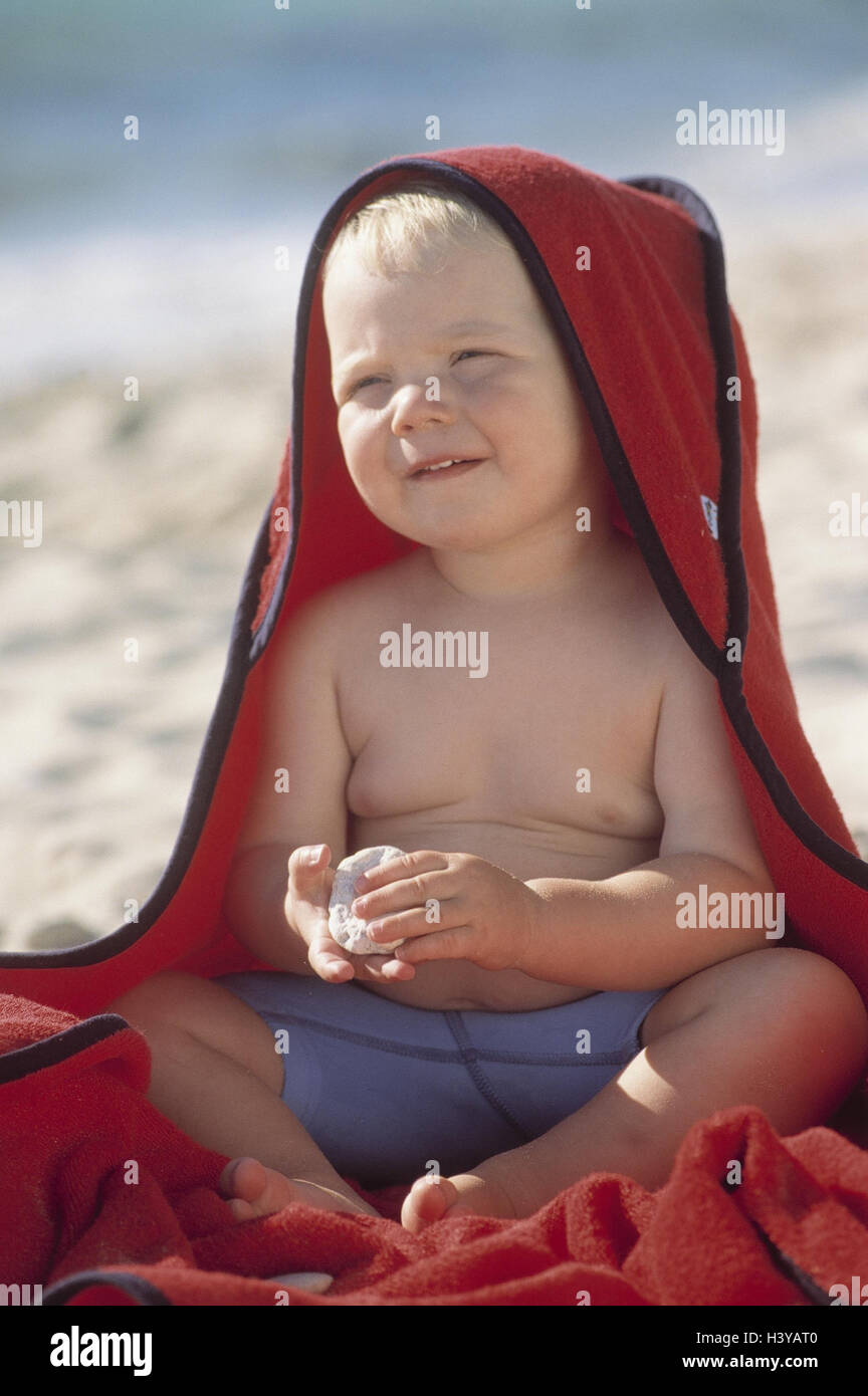 Beach, sea, boy, bath towel, wrapped, outside, summer, water, leisure time, vacation, holidays, childhood, infant, 18 months, happy, smile, wink carefully, attention, faded out, hood, headgear, sunscreen Stock Photo