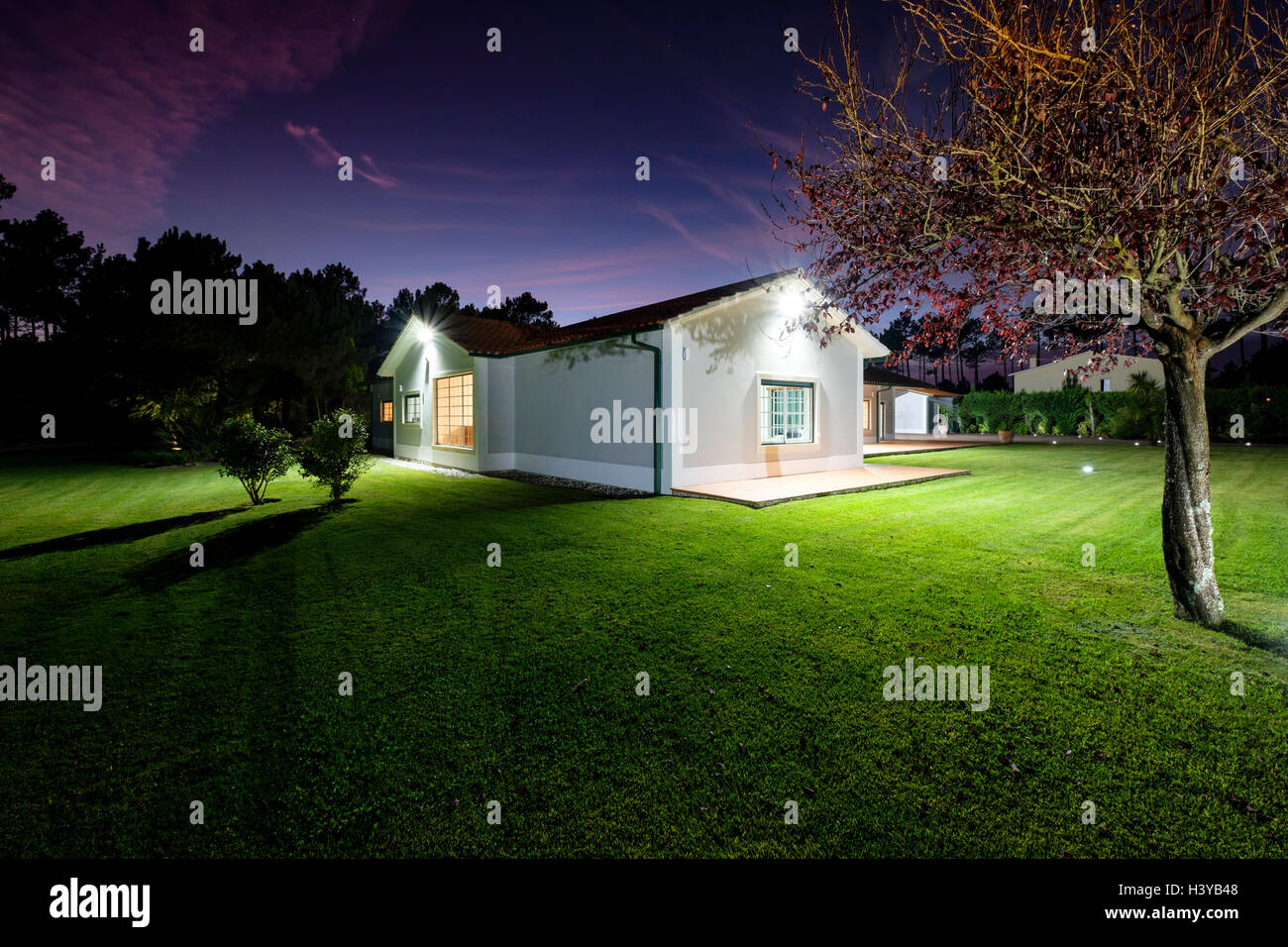 Dusk view of a modern illuminated house with big lawn Stock Photo - Alamy