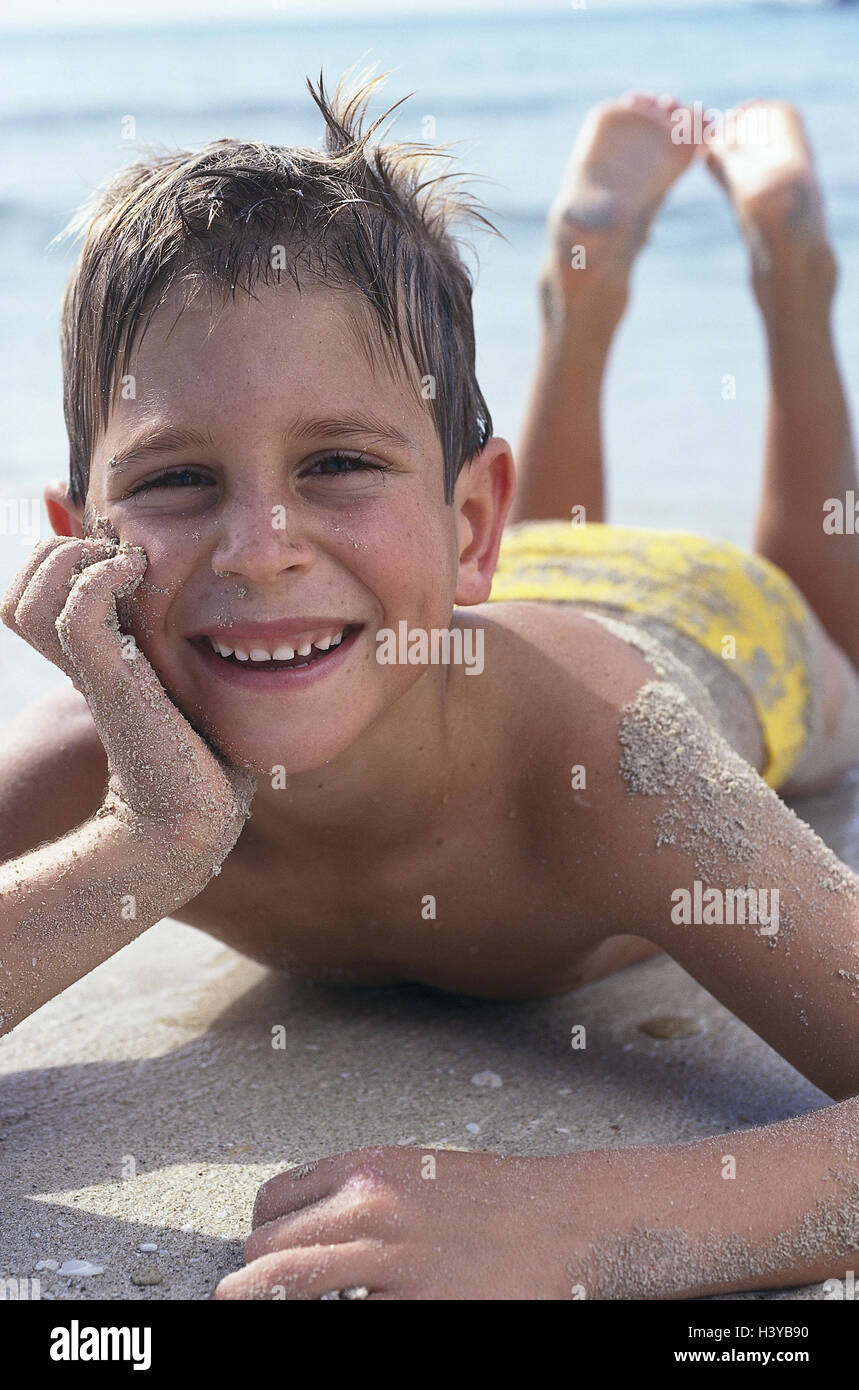 Beach, boy, swimming trunks, lie, smile, happy, very close, summer, outside, sandy beach, Sand, sea, vacation, holidays, leisure time, childhood, child, 7 years, happy, expression, mood, positively, swimwear, beach holiday, sandy, silts up Stock Photo