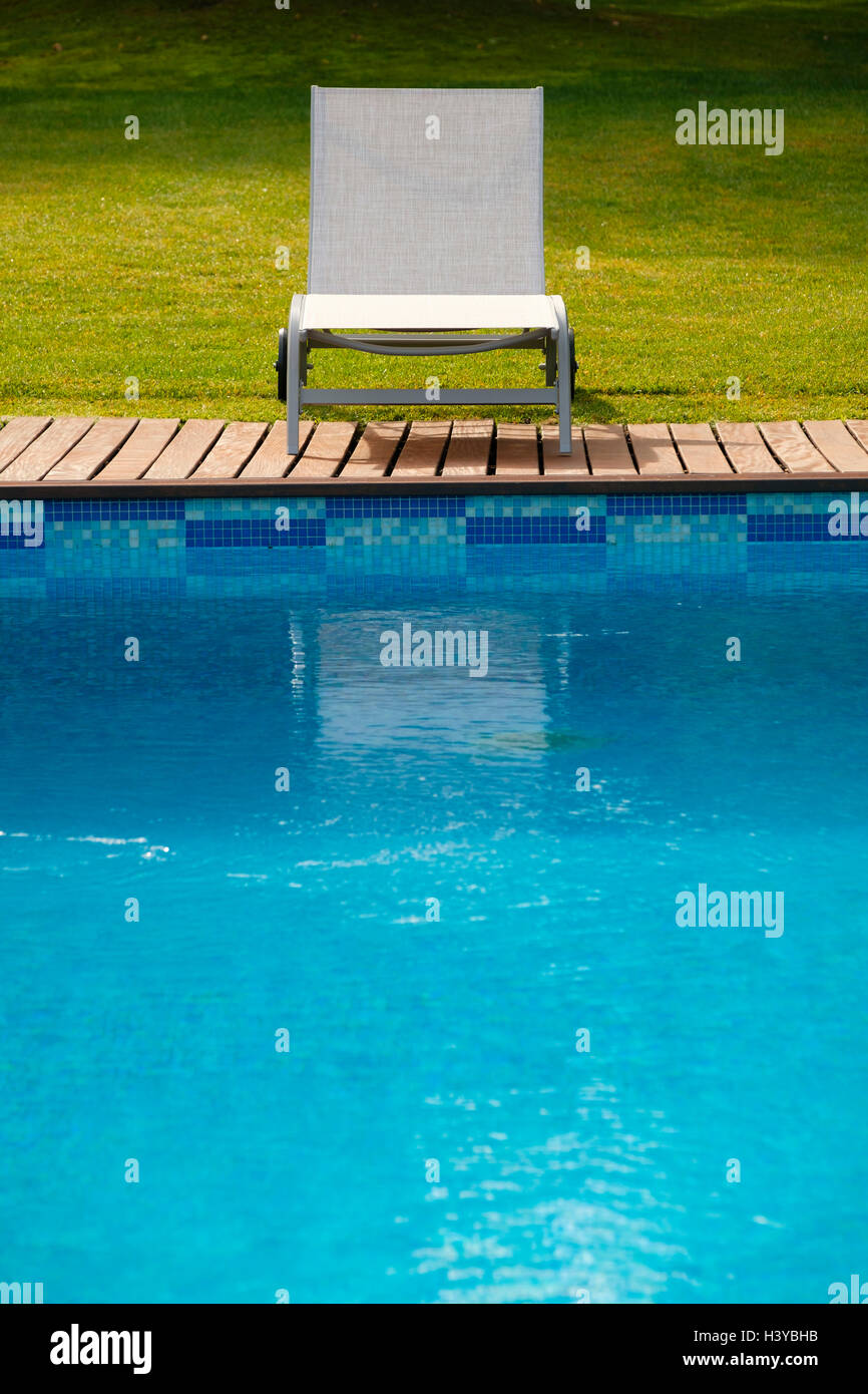 Sun lounger on wooden deck next to an outdoor swimming pool Stock Photo