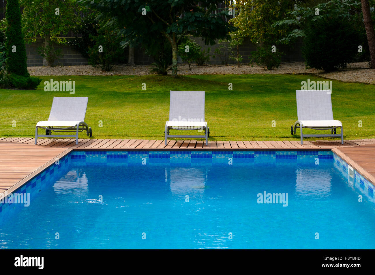 Sun loungers on wooden deck next to an outdoor swimming pool Stock Photo