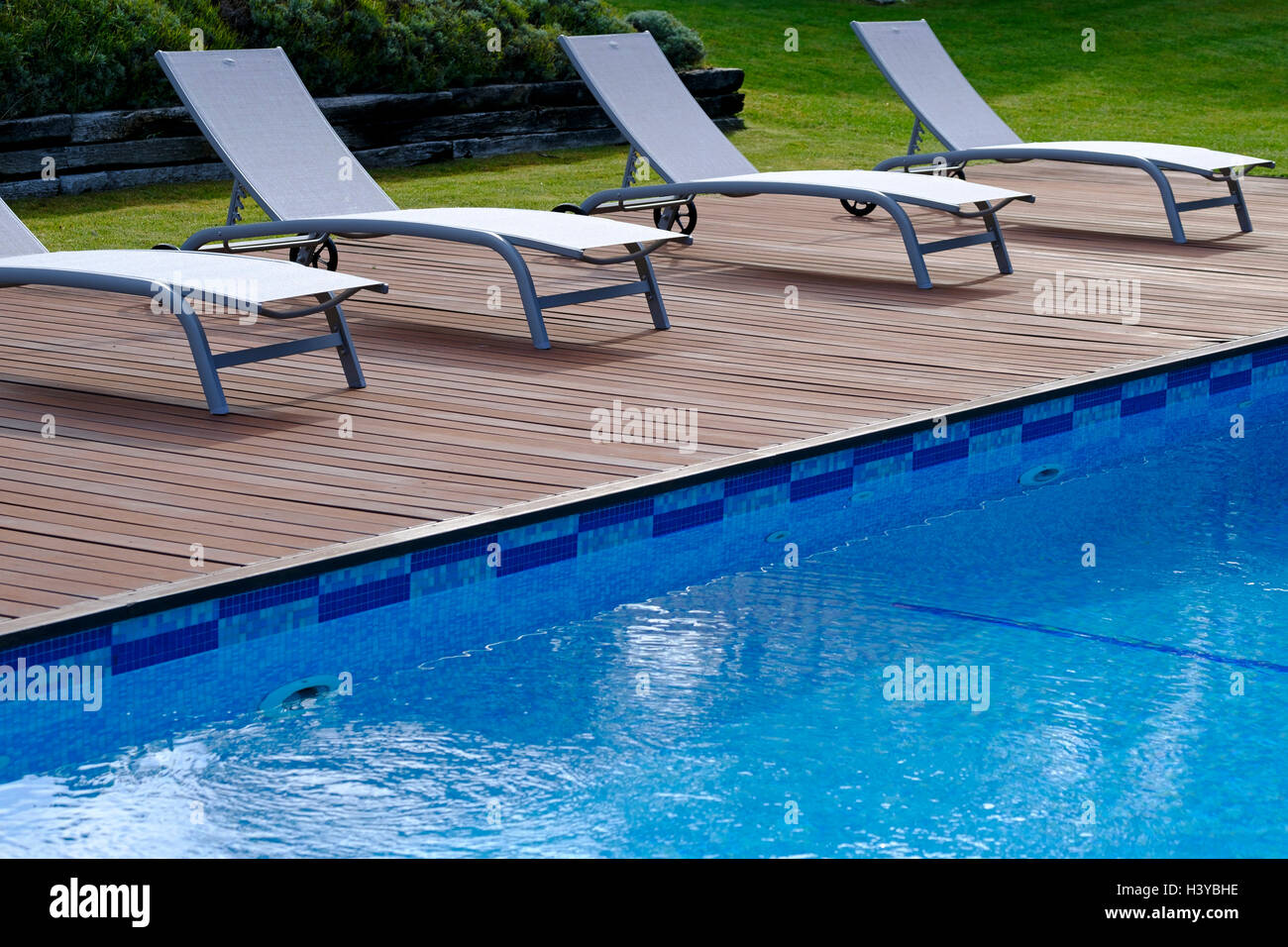 Lounge chairs on wooden deck next to an outdoor swimming pool Stock Photo