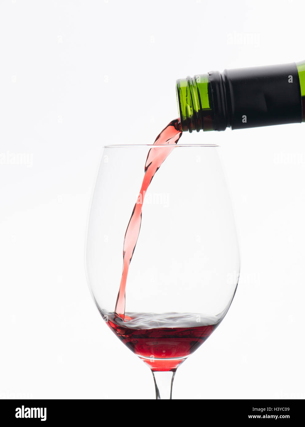 Red wine pouring from bottle in wineglass. Isolated on white background. Stock Photo