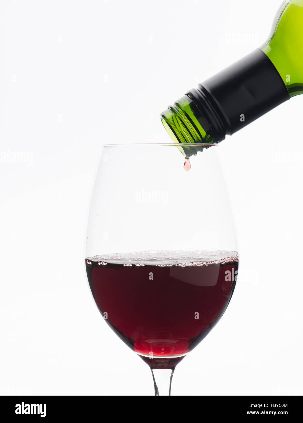 Last drop of red wine from bottle dripping down in wineglass. Isolated on white background. Stock Photo