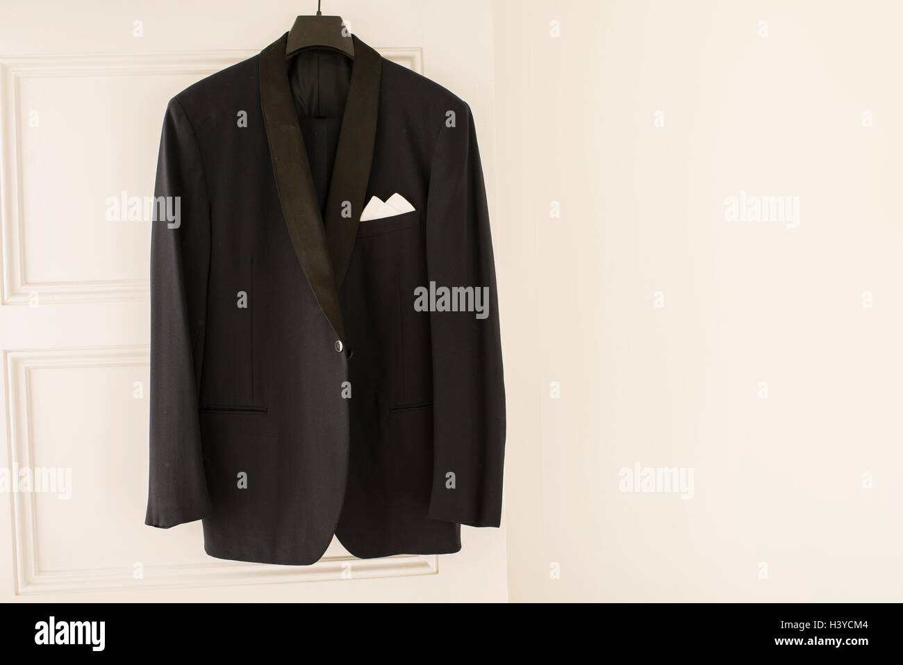 Black dinner jacket hanging from door on clothes hanger in empty white