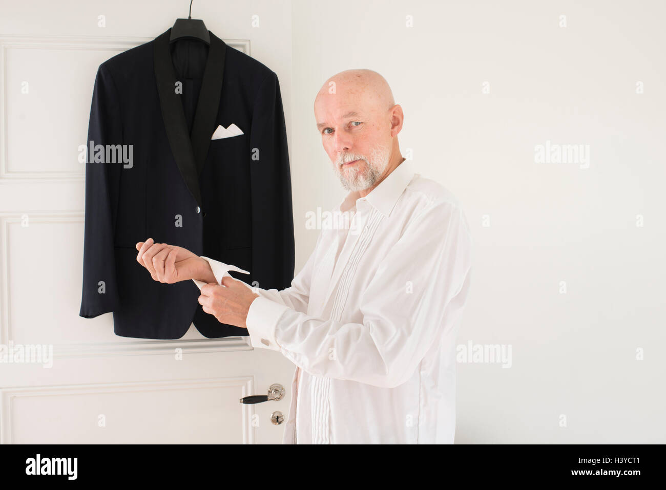 Old man putting on clothes at home, dinner jacket hanging in the background. Lifestyle moment of active retirement. Stock Photo